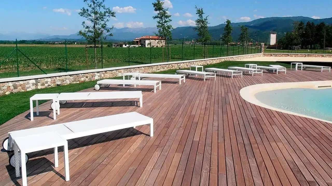 Velika lesena terasa z belimi ležalniki ob bazenu.