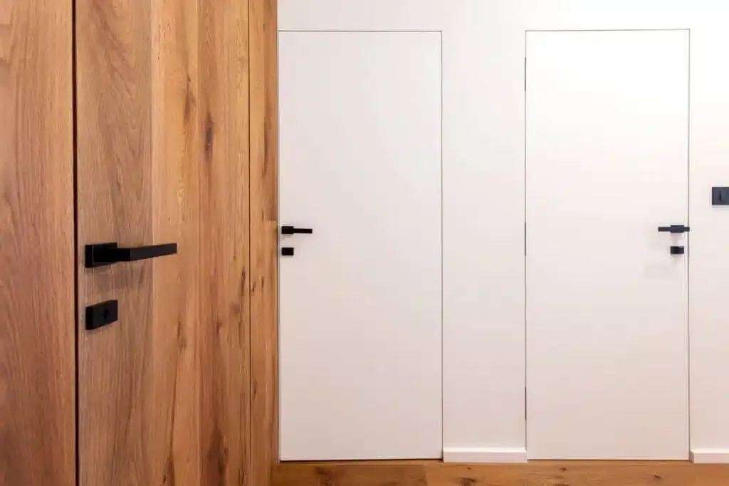 Bela vrata brez vidnih podbojev ob hrastovem vratnem krilu s črnim ročajem.